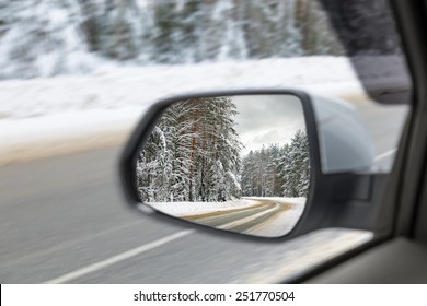 Side view mirror reflection of Snow-covered road in forest