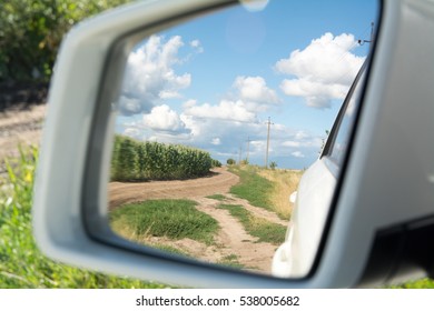Side view mirror reflection of two-lane winding road in field