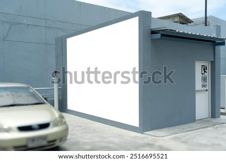 Side view of Mockup blank square billboard placed beside fire exit door on concrete structure in car park area, ready for advertisements.