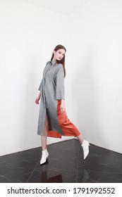 Side View Of A Model Which Is Turning Around To Look At Her Side. Tall Slender Caucasian Brunette Model Wearing Long Loose Clothes, Walking Indoors. Studio Photography, White Walls Background