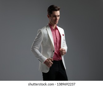 Side View Of A Modern Man In Suit Opening Or Closing His Lounge Jacket While Looking Away On Grey Background