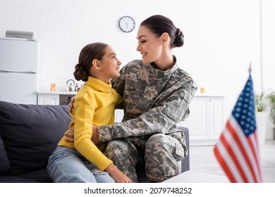 Side View Of Mom In Military Uniform Hugging Child Near American Flag On Table At Home