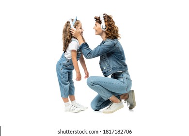 Side View Of Mother And Daughter In Denim Outfits Listening Music In Headphones Face To Face Isolated On White