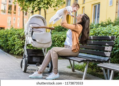 side view of mother holding happy baby on bench near stroller
