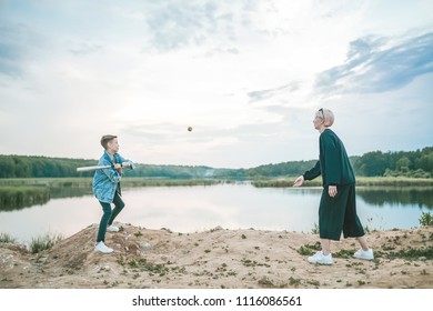 Side View Of Mother And Son Playing With Baseball Bat And Ball Near Lake