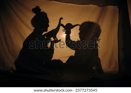 Side view of mother and son sitting behind curtain and playing with dinosaurs toys in shadow theatre