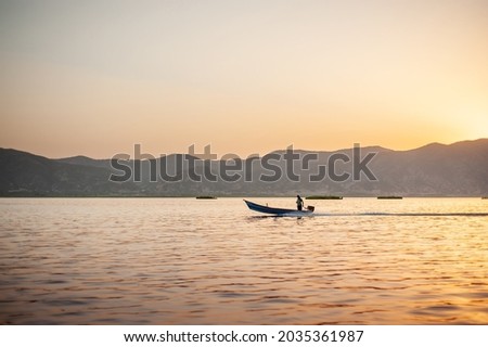 side view of a a motor boat cruising on the lake with man driving, mountain in background and water in foreground at sunset