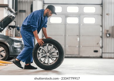 Side view. Moving the new tire. Auto mechanic working in garage. Repair service. - Powered by Shutterstock