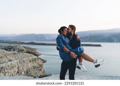 Side view of multiethnic couple near sea while standing on rocky cliff with eyes closed and enjoying happy time while male holding and kissing gently on forehead of mixed race female in hands - Powered by Shutterstock