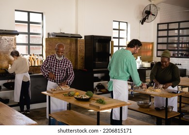 Side view of a multi-ethnic group of Senior adults at a cookery class, standing at wooden tables and preparing food in a restaurant kitchen - Powered by Shutterstock