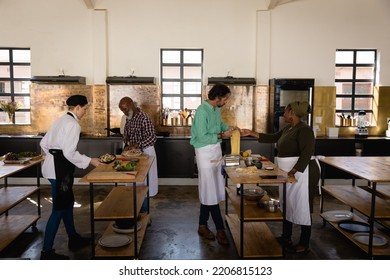 Side view of a multi-ethnic Senior group of adults at a cookery class, standing at wooden tables and preparing food, assisted by a Caucasian female chef wearing chefs whites and a black hat and apron - Powered by Shutterstock