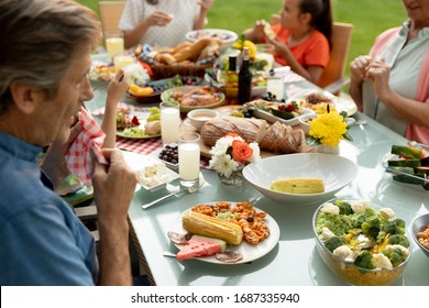 Side View Of A Multi-generation Caucasian Family Sitting Outside At A Dinner Table Set For A Meal, Eating. Family Enjoying Time At Home, Lifestyle Concept