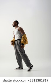 Side view of muscular african american man in bomber jacket and sleeveless t-shirt standing on grey background, contemporary shoot featuring stylish attire, fashion statement