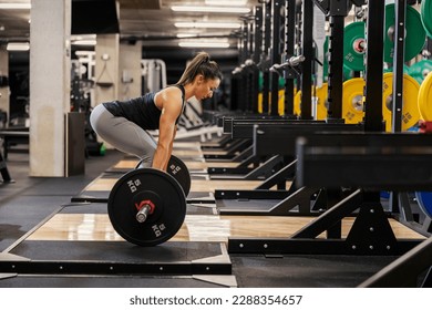 Side view of a muscular sportswoman in shape doing deadlifts with barbell in a gym. - Powered by Shutterstock