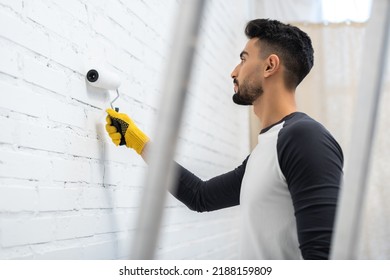 Side View Of Muslim Man Painting White Brick Wall At Home