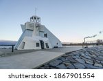 side view of Nallikari lighthouse in Oulu, Finland at Baltic sea. Maritime tower at the end of stone paved pier with smoke of a factory in the background. cloudless sky