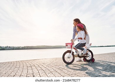 Side view. Near the lake. Mother with her young daughter is with bicycle outdoors together. - Powered by Shutterstock