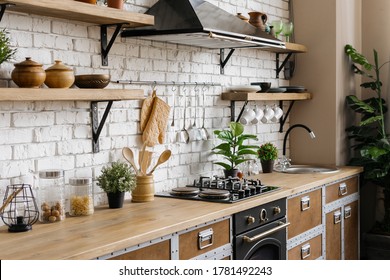Side view of new furniture, wooden countertop, gas stove, built in oven equipment, cooking hood, kitchenware supplies, houseplant in flower pot at kitchen in apartment with modern interior