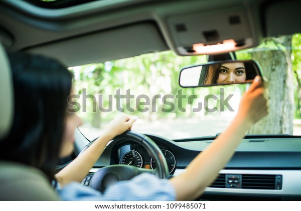 Side view of nice stylish girl\
touching a rear view mirror and smiling while driving the\
car