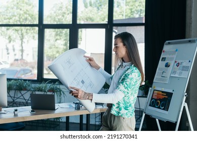 Side View Of Nonbinary Designer Holding Blueprint In Creative Agency