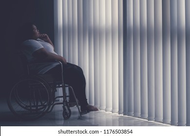 Side View Of Obese Woman Looks Pensive While Sitting In The Wheelchair By The Window. Shot In The Hospital  