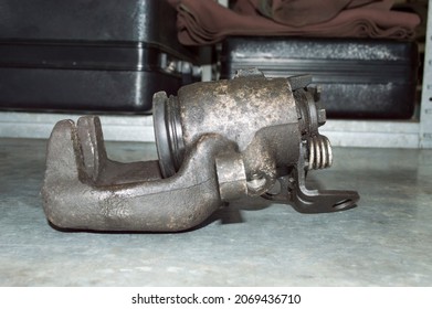 Side View Of An Old Car Brake Caliper, Which Lies On A Gray Metal Work Table In An Auto Repair Shop