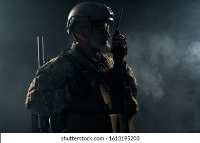 Side View Of Old Military Soldier In Uniform Holding Portable Radio Station In Smoke. Close Up Of Male Commander In Camouflage Uniform Giving Orders In Dark Atmosphere. Concept Of Army, Military.