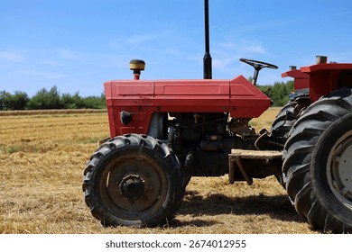 Side view of an old, red tractor with visible engine parked on the mowed wheat field