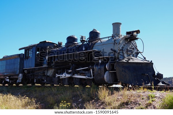 Side view of an old steam locomotive engine and one\
of it\'s cars.
