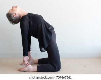 Side View Of Older Woman With Short Grey Hair And Black Clothing In Yoga Back Stretching Posture