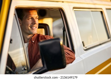 Side View On caucasian happy man looking at side through the window of yellow van, smiling during trip. handsome guy is travelling, alone. on road at sunset at summer day in nature