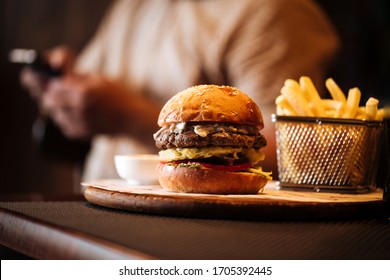 Side view on fast food combo set with appetizing burger and fries on the wooden board with blurry male on the background, horizontal format - Shutterstock ID 1705392445