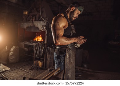 side view on forger man holding smartphone, having rest at work place. blacksmith shop owner, leisure time - Powered by Shutterstock