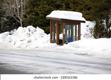 Side View On A Mountain Bus Stop And Wood Shelter Covered In Snow, Along An Icy Road,