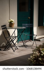 Side View On An Outdoor Sitting Area, With Black Table And Chair Patio Furniture,  In A Sunny Courtyard