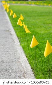 Side View On A Row Of Yellow Marker Flags For A Buried Natural Gas Line In A Grass Lawn, Along  A Concrete Sidewalk, With Space For Text On The Left 