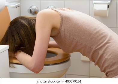 Side view on sick young woman wearing sleeveless shirt in leaning on open toilet seat at indoor bathroom