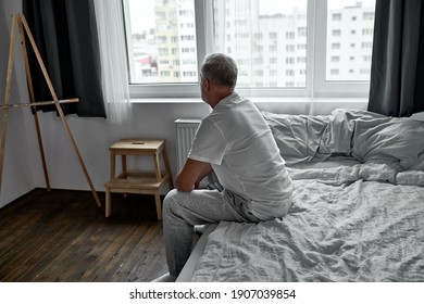 Side View On Upset Man Sitting Alone On Bed At Home In Dark Room, Morning Alone.