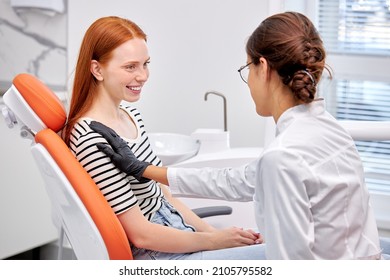 Side View On Young Professional Female Dentist Calming Patient Down Before Treatment, Attractive Redhead Caucasian Woman Is Smiling, Having Conversation, Discussing. Healthcare, medicine concept