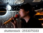 side view of one Asian young woman holding microphone, singing karaoke in KTV