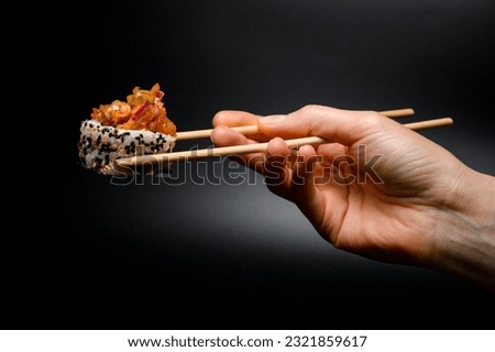 side view of one piece of roll with caramelized onion, raw fish, sesame and rice in hand holding with wooden chopsticks.