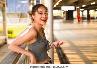 Side View Of One Sexy Slim Pretty Young Asian Girl Looking At Camera Smile With Mobile Phone In Hand At Summer Afternoon Sunlight In The Urban City Street