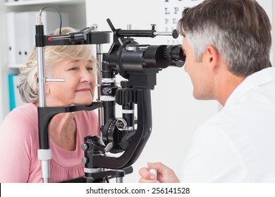 Side view of optician examining senior female patient through slit lamp in clinic