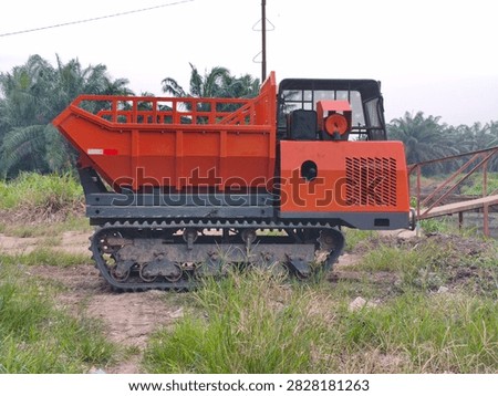Side view of an orange tracked crawler dumper parked on a palm oil plantation