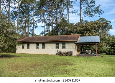 Side View Of Outdoor Storage Building Shed Made Of Stucco And Cinder Block Walls With A Regular And Metal Roof Overhang With A Pile Of Wood For The Winter.