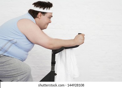 Side View Of An Overweight Man On Exercise Bike Against White Background