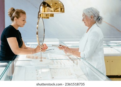 Side view of owner and senior woman shopping at jewelry shop. Elderly female paying with smartphone, scan and pay bill on card machine making quick easy contactless payment. NFC technology concept. - Powered by Shutterstock