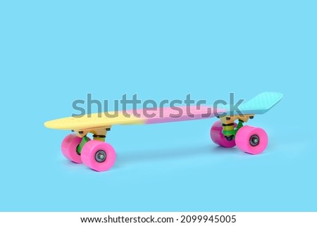 Side view of pastel neon rainbow colored Penny board skateboard isolated on solid blue background. Plastic mini cruiser. Youth minimalistic Sport inspired summer fun concept. Copy space.