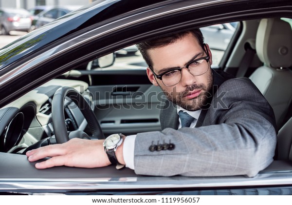 side view of pensive businessman in\
eyeglasses looking away while driving\
car