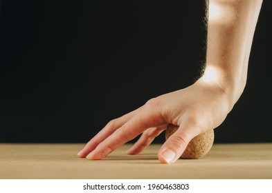 Side view of person doing palmar fascia release with a small cork ball on a black background with golden light, with copy space